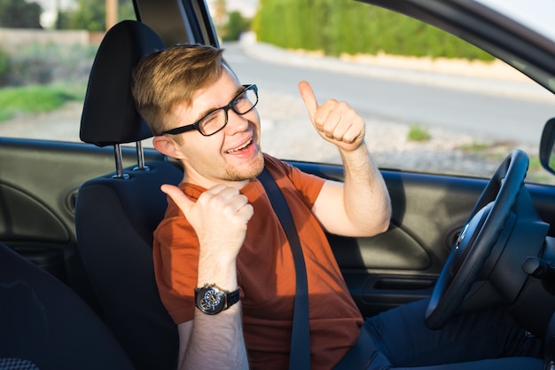 Gelukkig jonge man zit in de auto en toont duimen omhoog.