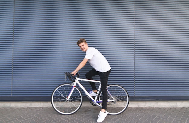 Gelukkig jonge man zittend op een witte fiets tegen de muur