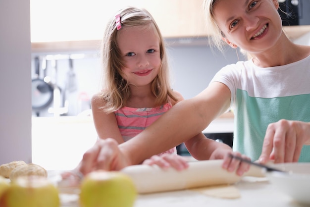 Gelukkig jonge moeder en dochtertje van klein kind rolt deeg op keukentafel met pin