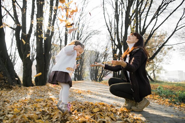 Foto gelukkig jonge moeder met haar kleine babymeisje spelen met herfstbladeren