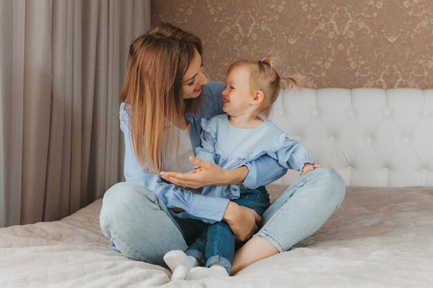 Gelukkig jonge moeder speelt met haar dochter op het bed thuis. Moederdag.