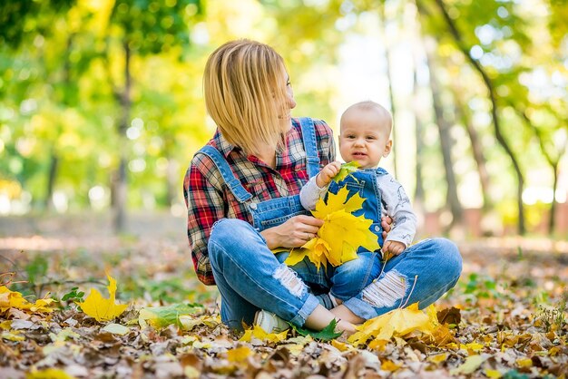 Gelukkig jonge moeder spelen met baby in herfst park met gele esdoorn bladeren.