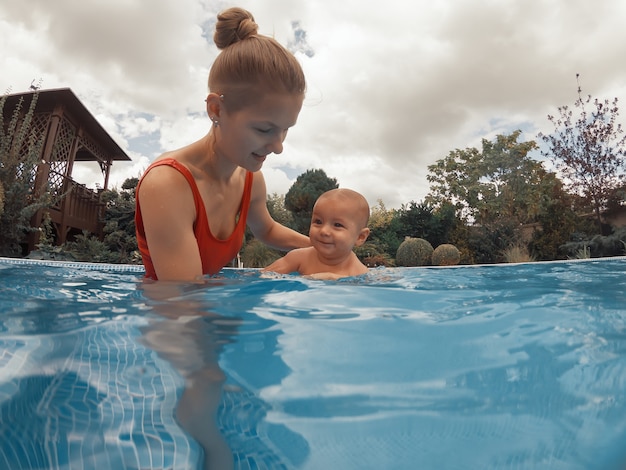 Gelukkig jonge moeder spelen met haar baby in het buitenzwembad op een warme zomerdag