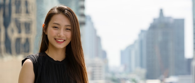Gelukkig jonge mooie Aziatische zakenvrouw tegen uitzicht over de stad