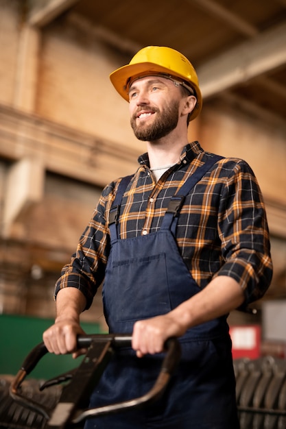 Foto gelukkig jonge professionele technicus in veiligheidshelm en overall met behulp van technisch handgereedschap in werkproces