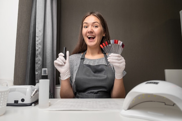 Gelukkig jonge vrouw beroep manicure met Pools en nagel kleurenpalet op grijze achtergrond