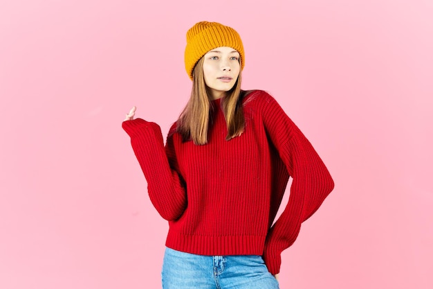 Foto gelukkig jonge vrouw dragen warme trui en gebreide muts op roze achtergrond meisje winter portret lachende hipster met bretels plezier