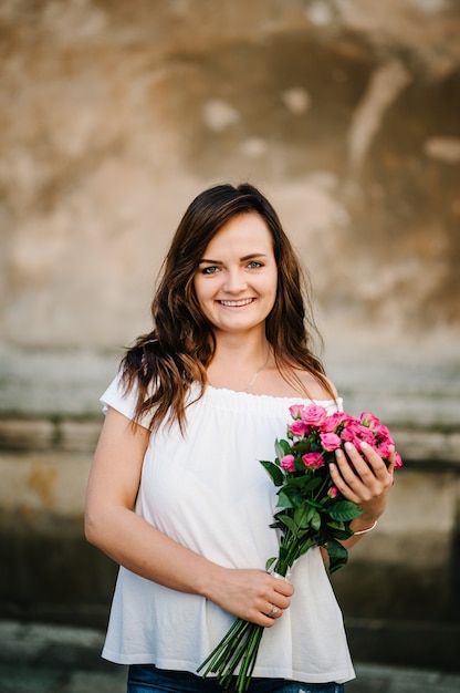 Gelukkig jonge vrouw houdt een boeket roze rozen, die zich voordeed op camera, t-shirt dragen. Buitenshuis. Lente portret van mooie vrouw in park.