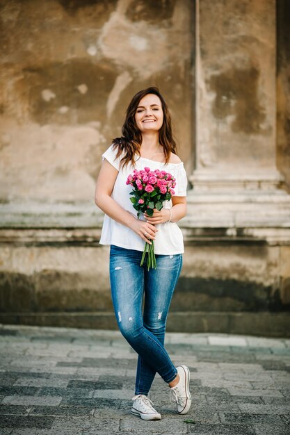 Foto gelukkig jonge vrouw houdt een boeket van roze rozen die zich voordeed op camera dragen tshirt outdoors lente portret van mooie vrouw in park