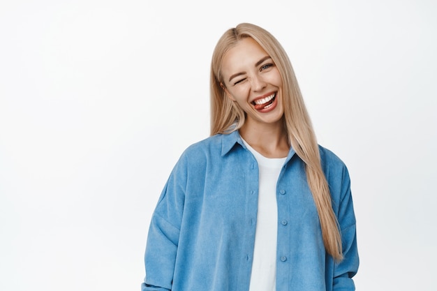 Gelukkig jonge vrouw knipogen, glimlachen en tong, dwaze en speelse emotie tonen, staande op wit.