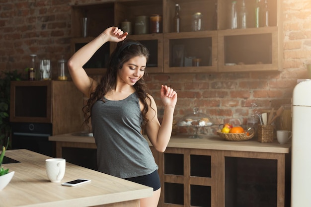 Gelukkig jonge vrouw koffie drinken en luisteren naar muziek op smartphone in loft keuken. Vroege ochtend, ontbijt, leuk concept