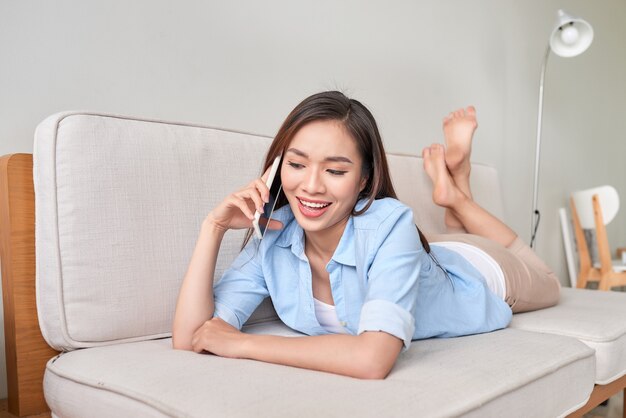 Gelukkig jonge vrouw liggend op de bank thuis, praten aan de telefoon met vriend