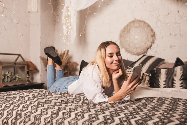 Gelukkig jonge vrouw ligt op het bed op kerstavond en spreekt aan de telefoon.