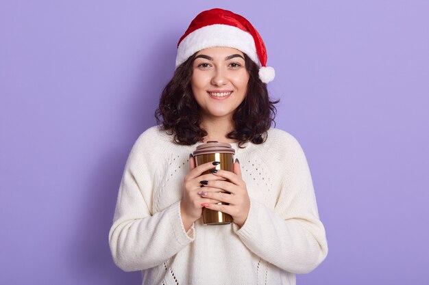 Gelukkig jonge vrouw met kerstmuts koffie drinken uit thermomok