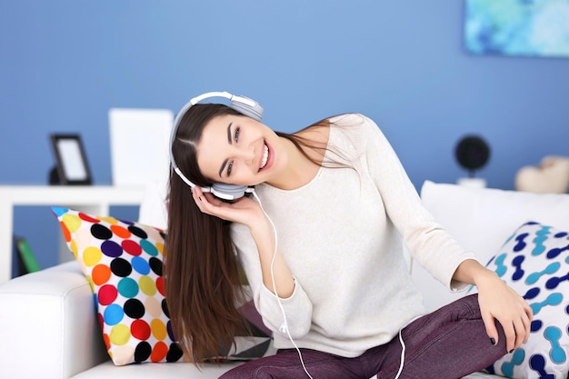 Gelukkig jonge vrouw met koptelefoon luisteren naar muziek op een sofa thuis