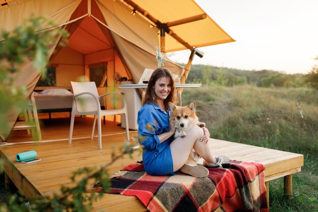 Gelukkig jonge vrouw met Welsh Corgi Pembroke hond ontspannen in glamping op zomerdag Luxe kampeertent voor openluchtrecreatie en recreatie Lifestyle concept