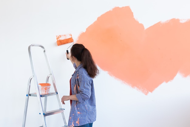 Gelukkig jonge vrouw schilderij muur in haar nieuwe appartement. Renovatie-, herinrichting- en reparatieconcept