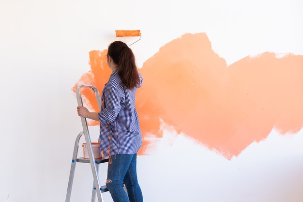 Gelukkig jonge vrouw schilderij muur in haar nieuwe appartement. Renovatie-, herinrichting- en reparatieconcept