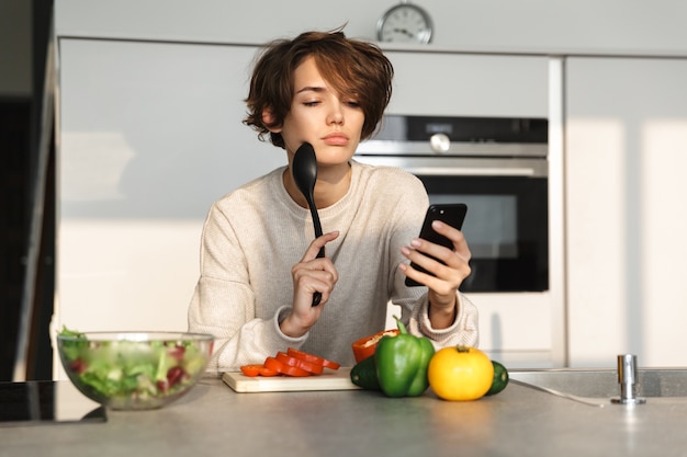 Gelukkig jonge vrouw verse salade koken in de keuken thuis