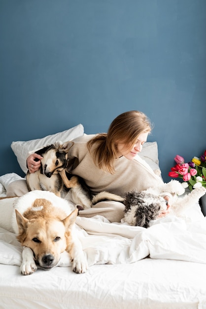 Gelukkig jonge vrouw zittend in het bed met haar honden, blauwe muur achtergrond