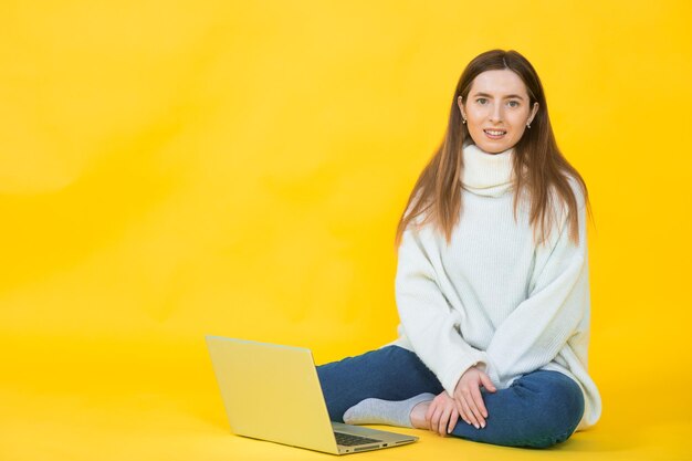 Gelukkig jonge vrouw zittend op de vloer met gekruiste benen en met behulp van laptop op geel