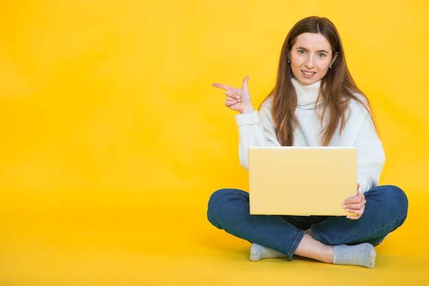 Gelukkig jonge vrouw zittend op de vloer met gekruiste benen en met behulp van laptop op geel