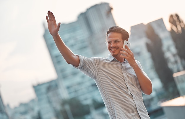 Gelukkig jonge zakenman praten op mobiele telefoon in de buurt van business center en zwaaien.