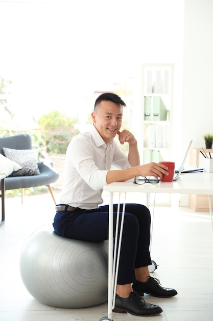 Gelukkig jonge zakenman zittend op fitness bal in office Workplace oefeningen