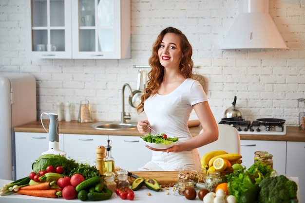 Gelukkig jongedame salade eten in de mooie keuken met groene verse ingrediënten binnenshuis. Gezond eten concept