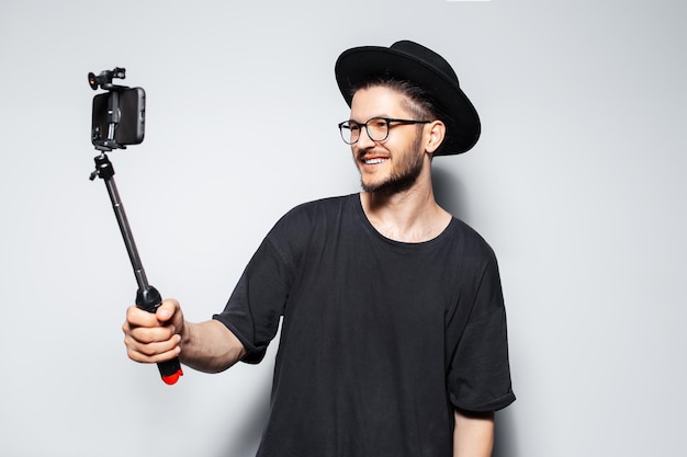 Gelukkig jongeman video maken door smartphone met selfie stick op grijze achtergrond