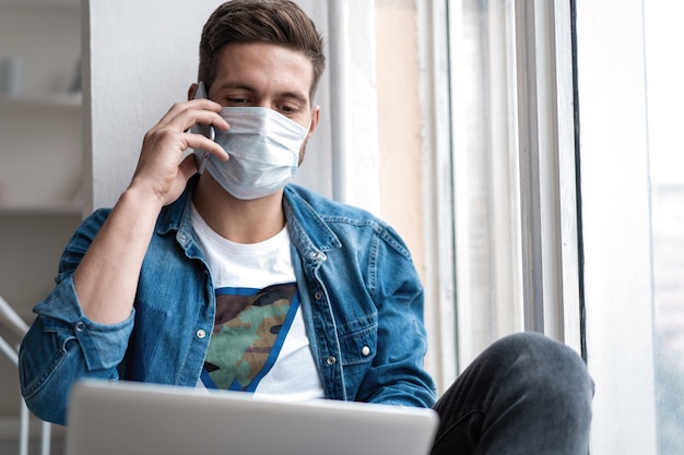 Gelukkig jongeman zit in beschermend masker praten aan de telefoon.