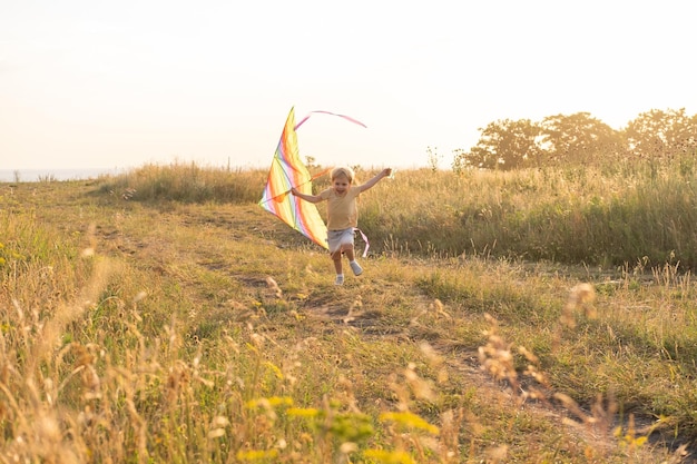 Gelukkig jongetje dat plezier heeft met vlieger in de natuur bij zonsondergang