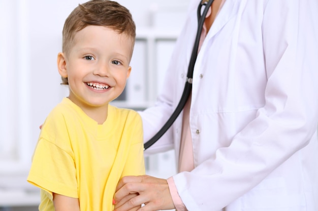 Gelukkig jongetje dat plezier heeft terwijl hij door een arts wordt onderzocht met een stethoscoop Gezondheidszorgverzekering en hulpconcept