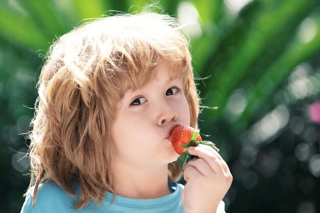 Gelukkig jongetje eet aardbeien op groene zomerachtergrond