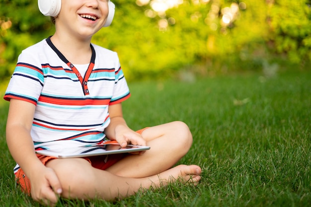 Gelukkig jongetje in draadloze koptelefoon met een tabletcomputer buiten in een zomerpark