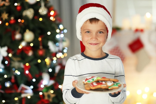 Gelukkig jongetje in kerstmuts met bord met koekjes thuis