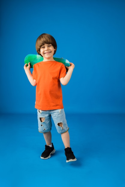 Gelukkig jongetje met bruin haar houdt een skateboard op een blauwe ondergrond met ruimte voor tekst