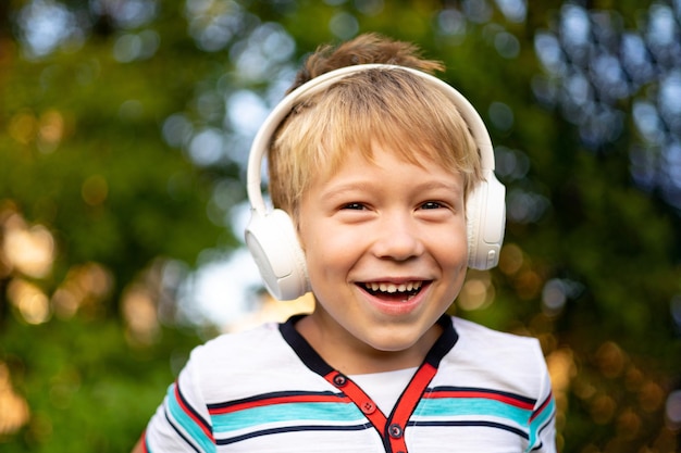 Gelukkig jongetje met draadloze koptelefoon buiten in een zomerpark lachend lachend
