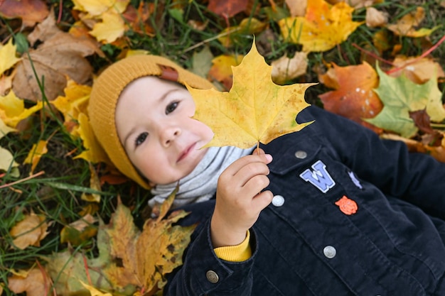 Gelukkig jongetje met een esdoornblad in zijn hand bovenaanzicht Jongen veel plezier en ligt op herfstbladeren