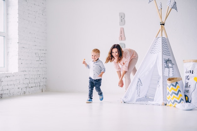 Gelukkig jongetje met snoep in zijn handen ontsnapt van zijn moeder in een lichte kamer met baby wigwam en eco-tassen