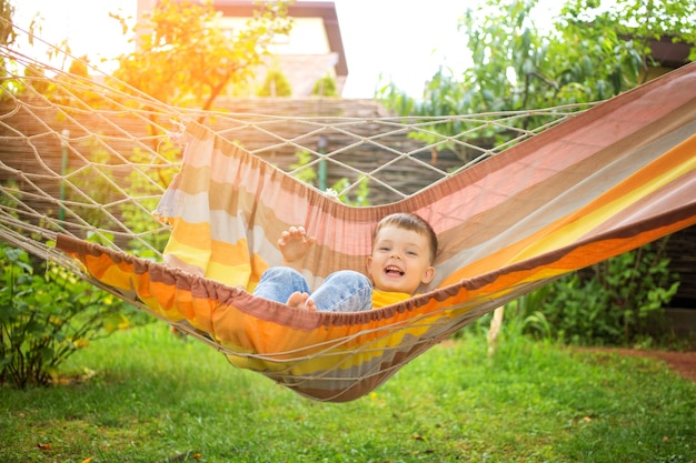 Gelukkig jongetje rijden in een lichte hangmat in zijn park. Zomer kindervakantie