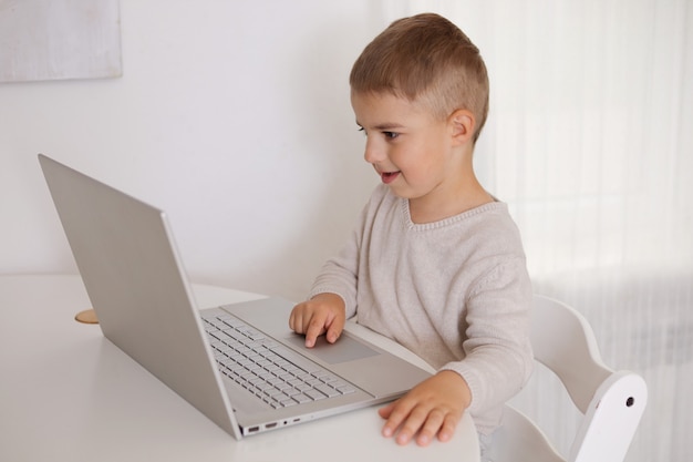 Gelukkig jongetje speelspel op laptop thuis. Portret van een kind dat thuis tekenfilm kijkt op de computer. Moderne technologie voor kinderen en onderwijs.