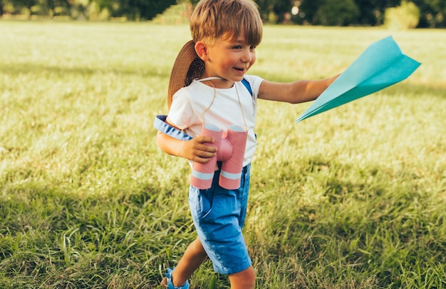 Gelukkig jongetje spelen met een verrekijker en papieren vliegtuigje in zomerdag in park Vrolijk kind buiten spelen op groen gras Jeugd concept