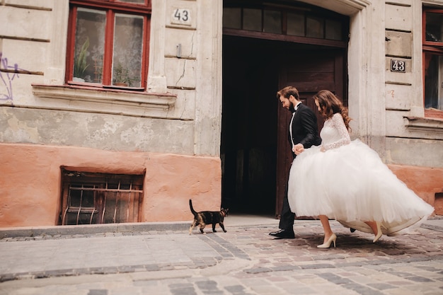 Foto gelukkig jonggehuwde paar knuffelen en zoenen in oude europese stad straat, prachtige bruid in witte trouwjurk samen met knappe bruidegom. trouwdag.