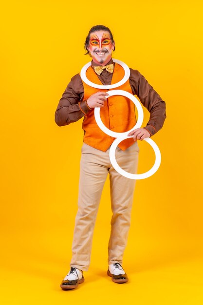 Gelukkig jongleur man in make-up vest jongleren met hoepels op een gele achtergrond