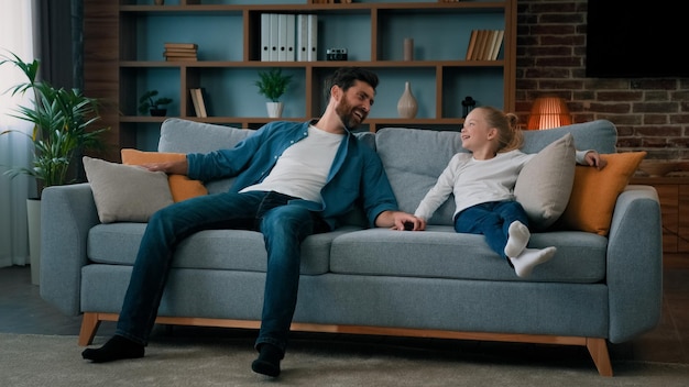 Gelukkig kaukasisch jong gezin papa en kind dochter springen op een zachte bank voor een pauze overdag