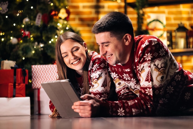 Gelukkig Kaukasisch paar dat thuis in de buurt van de kerstboom ligt als achtergrond mooie vrouw met lang haar