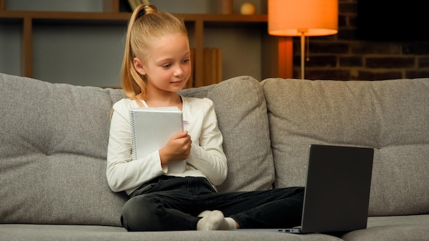 Gelukkig kaukasisch preteen meisje leerling klein kind zit in een gezellige houding op de bank afstandsonderwijs online