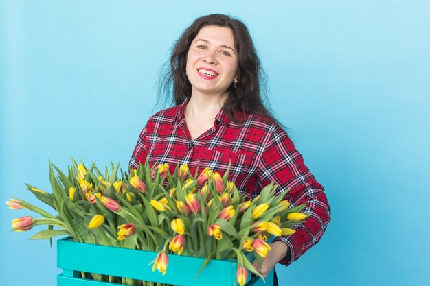 Gelukkig Kaukasische vrouwelijke bloemist lachen en houden grote doos tulpen op blauwe achtergrond