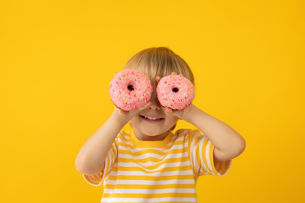 Gelukkig kind dat geglazuurde doughnut houdt tegen gele muur